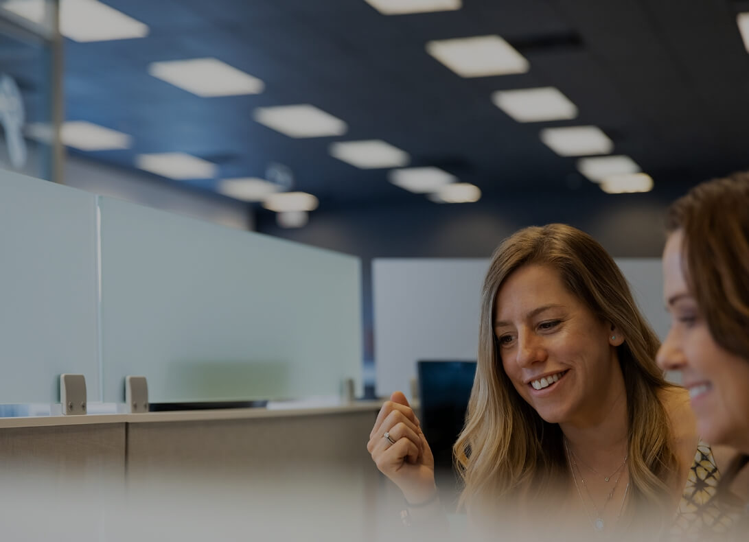 Two women sitting side by side at a desk, collaborating on work