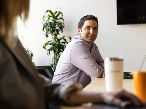 Side view of a woman sitting at a table in a conference room, looking at a coworker to her left and laughing