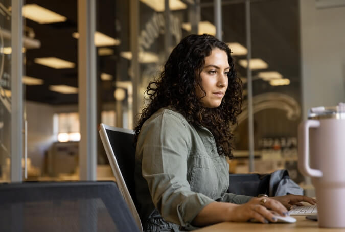 Woman sitting at a conference room table with glass walls behind her, focusing on her work