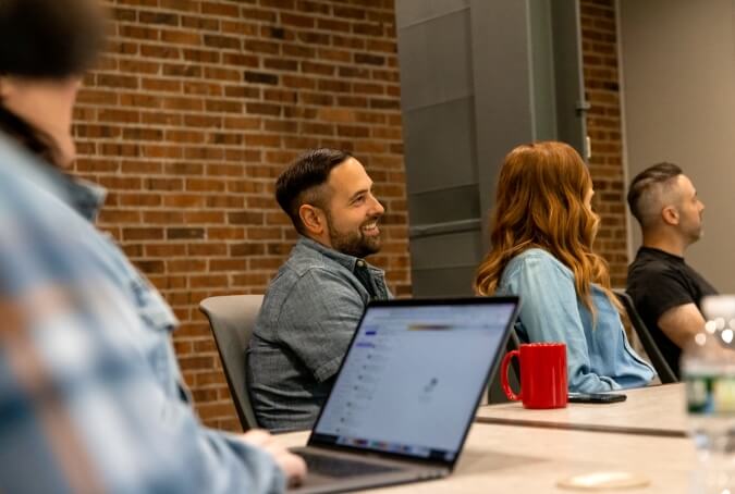 Three coworkers sitting on one side of a conference room table, watching a presenter out of frame to the right